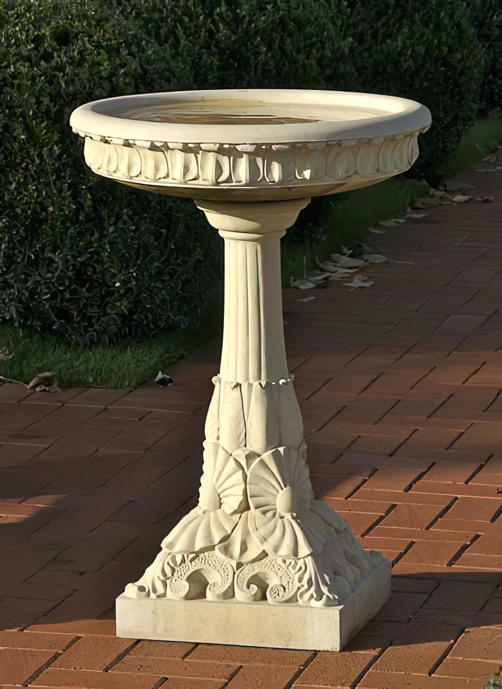 Abbeveratoio bianco in pietra con decorazioni scolpite in giardino su un sentiero lastricato