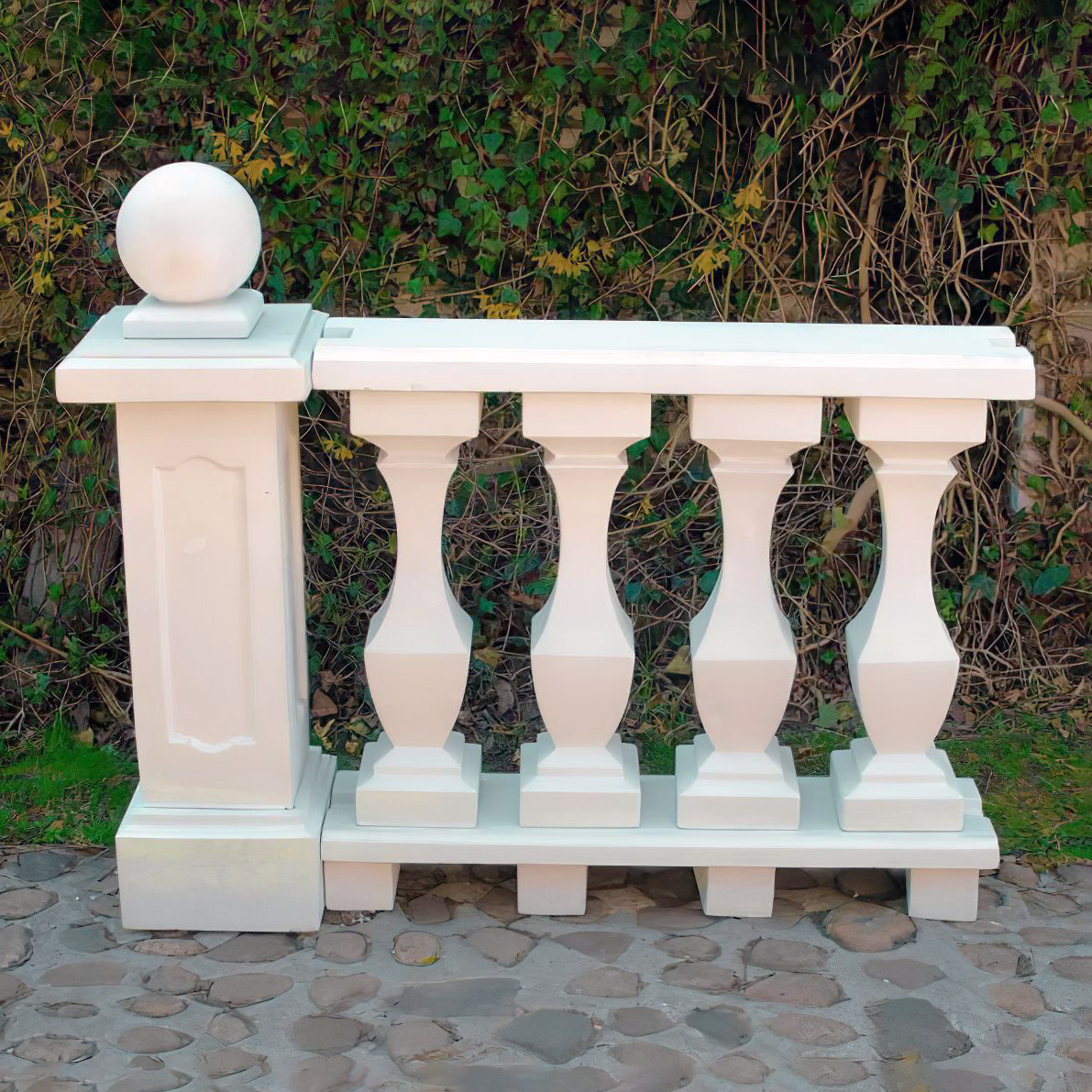 Balustrade décorative blanche en pierre dans un jardin devant un buisson vert