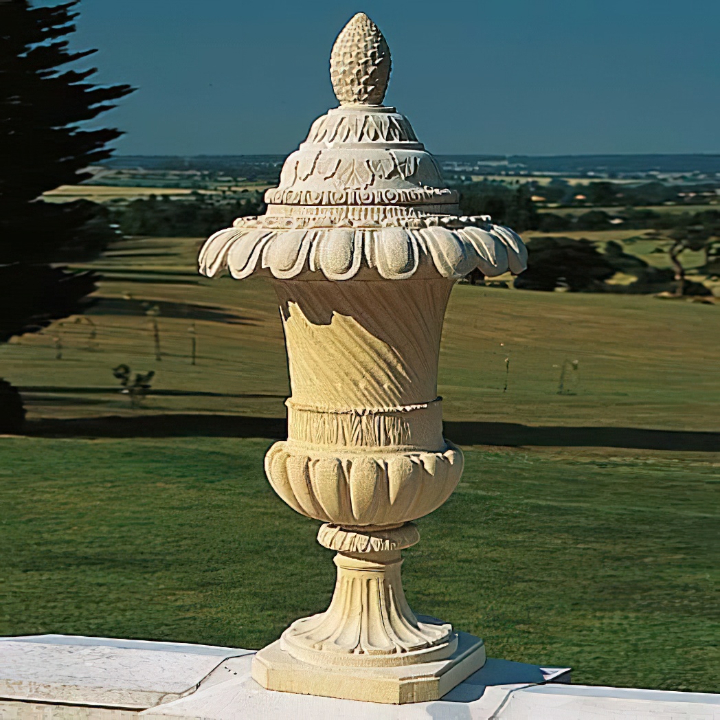 Kunstvolle Gartendeko aus Stein in Form einer Ananas auf einem Podest vor grüner Wiese
