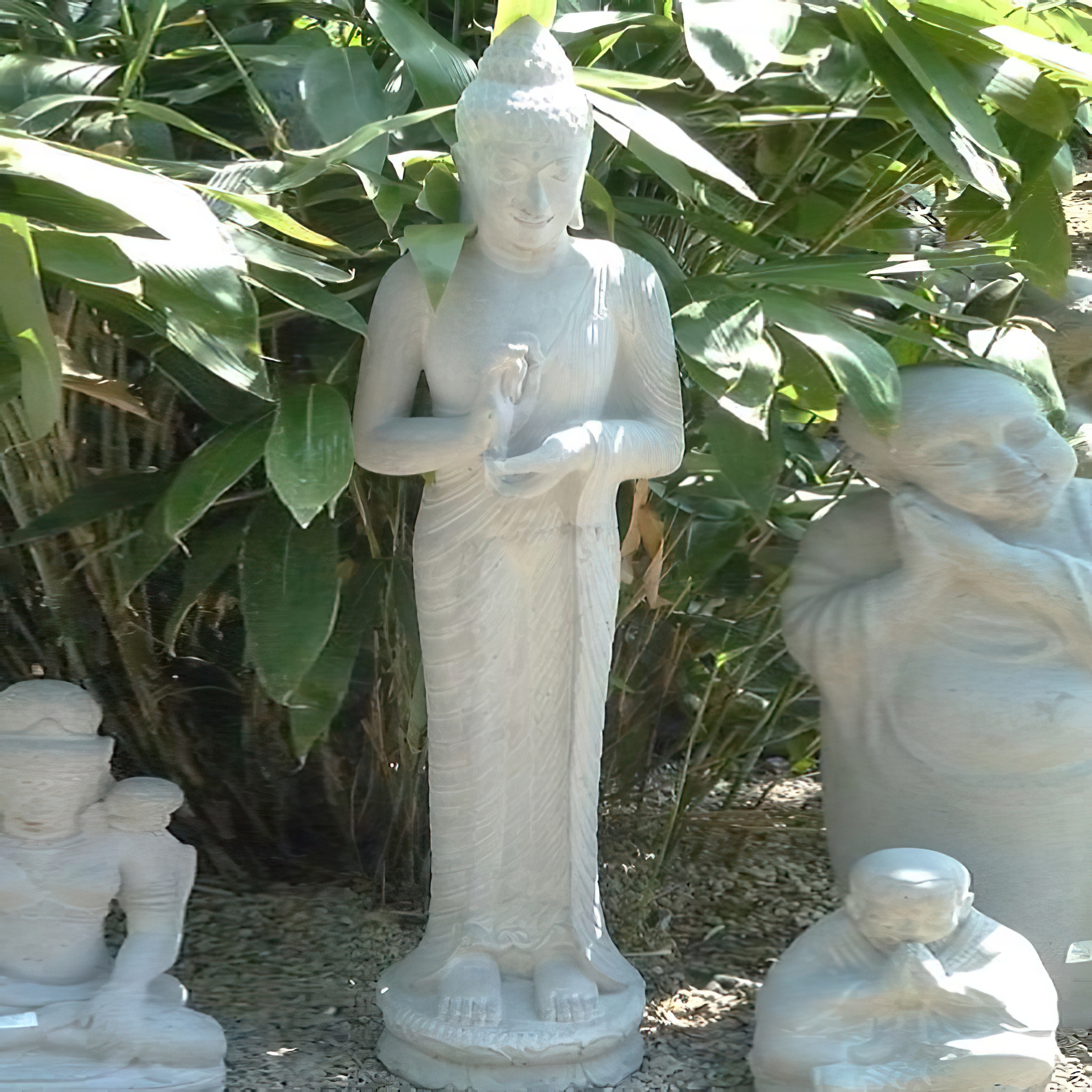 Sculpture en pierre de Bouddha entourée d'autres statues et de plantes vertes dans un jardin