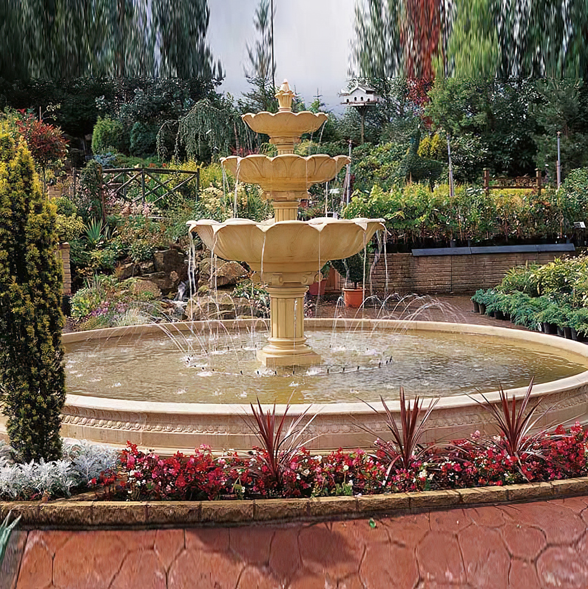 Grande fontana decorativa da giardino con più vasche d'acqua, circondata da piante e fiori nel giardino