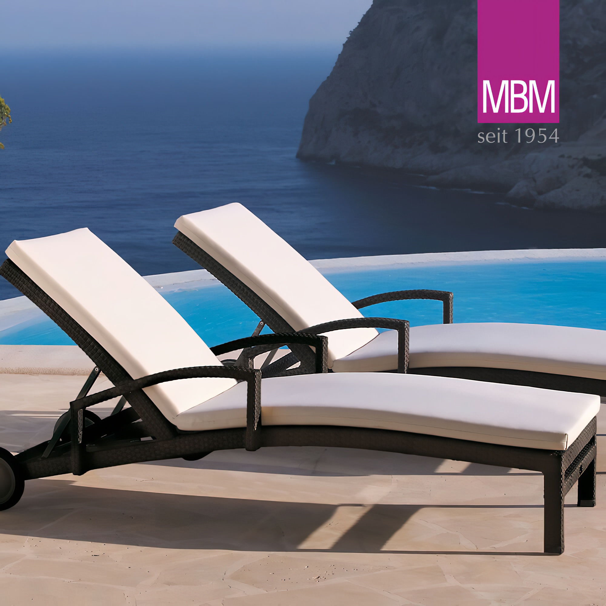 Zwei moderne Gartenliegen mit weißen Polstern neben einem Pool und Blick auf das Meer
