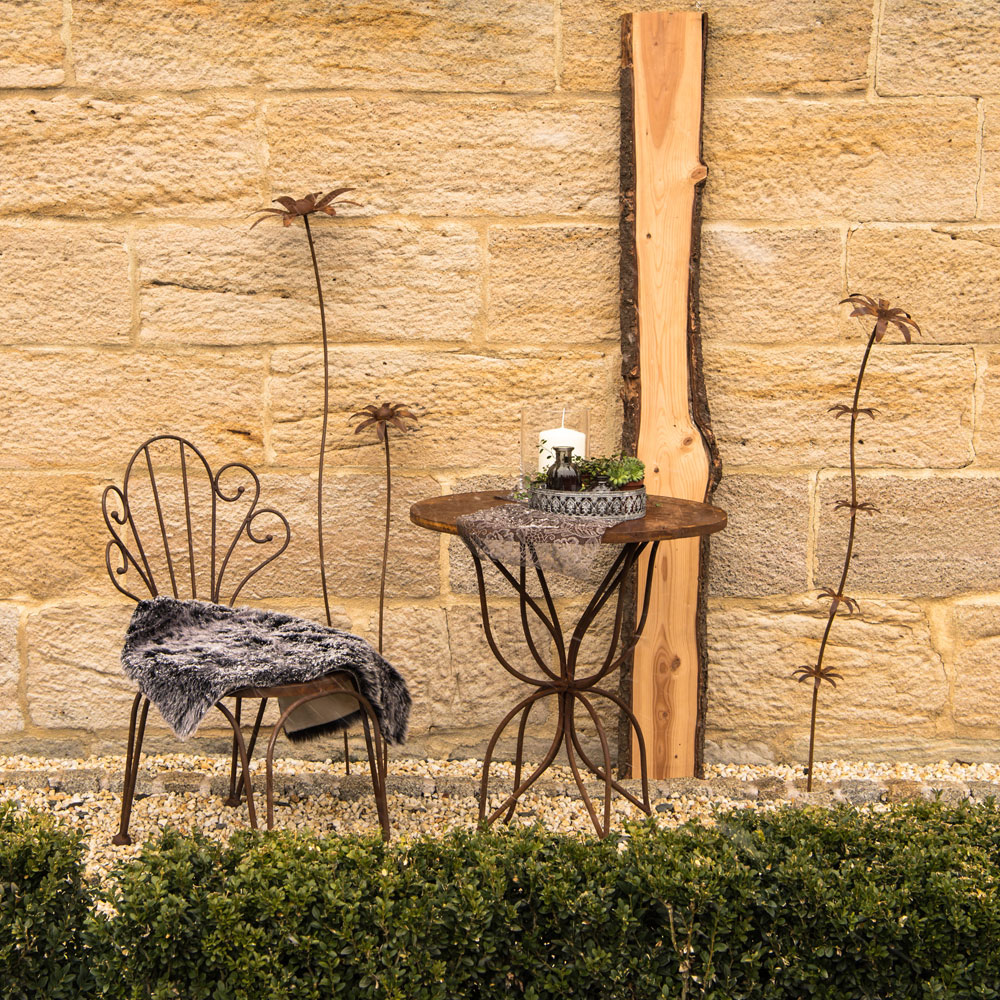 Chaise en métal noire avec coussin en fourrure et table de jardin en métal avec bougie devant mur en pierre