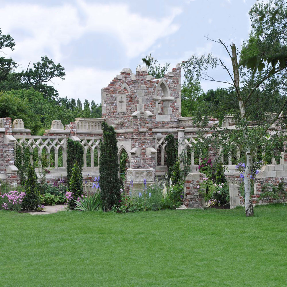 Ruine aus Steinmauer mit grünen Büschen und grasgrünem Garten im Vordergrund