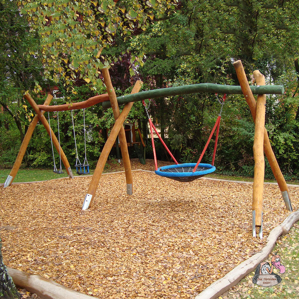Eine Holzschaukel mit blauer Sitzfläche in einem Garten mit Holzschnitzelboden und Bäumen im Hintergrund