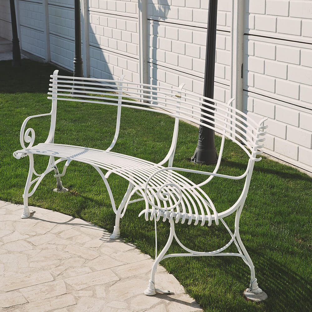Elegante weisse Gartenbank aus Metall auf Rasen vor weisser Mauer