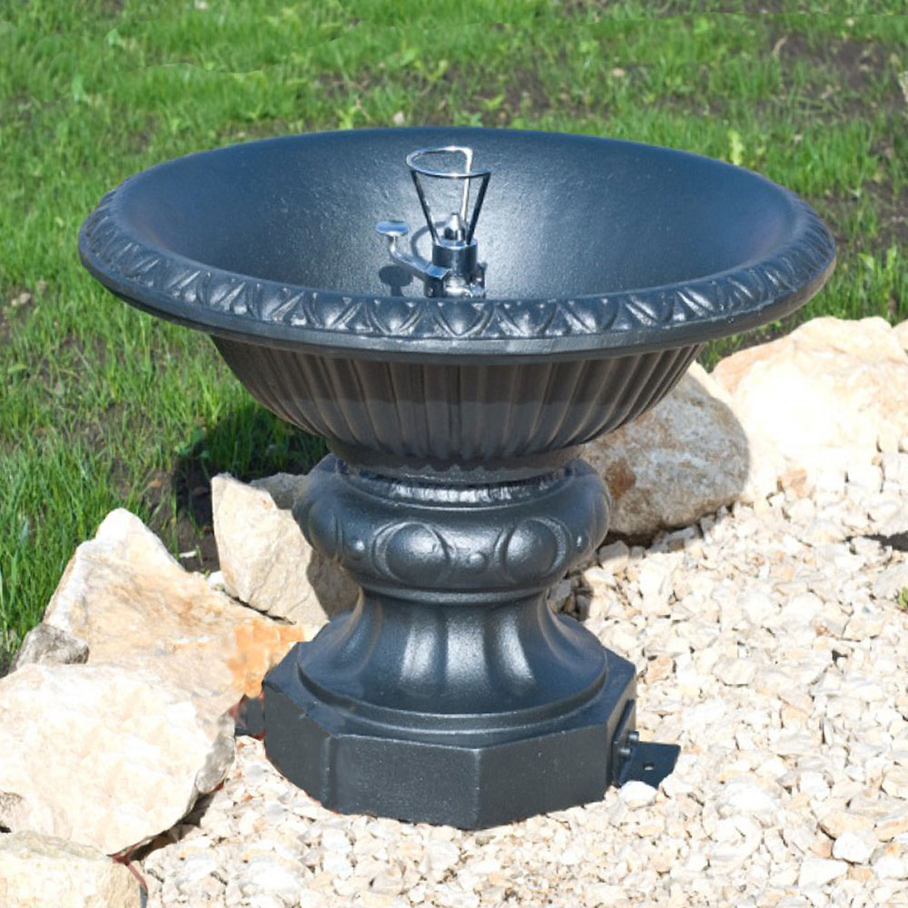 Moderner schwarzer Gartenbrunnen aus Metall steht dekorativ auf hellem Kies und Gras