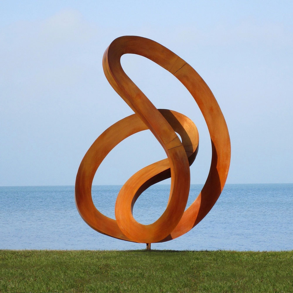 Rostfarbene abstrakte Skulptur auf grünem Rasen mit Meer im Hintergrund