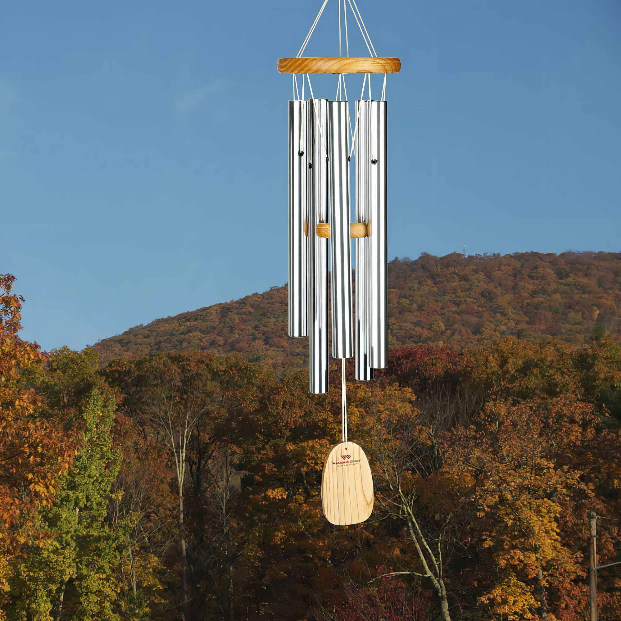 Carillon en bois et métal suspendu devant une forêt d'automne et un ciel bleu