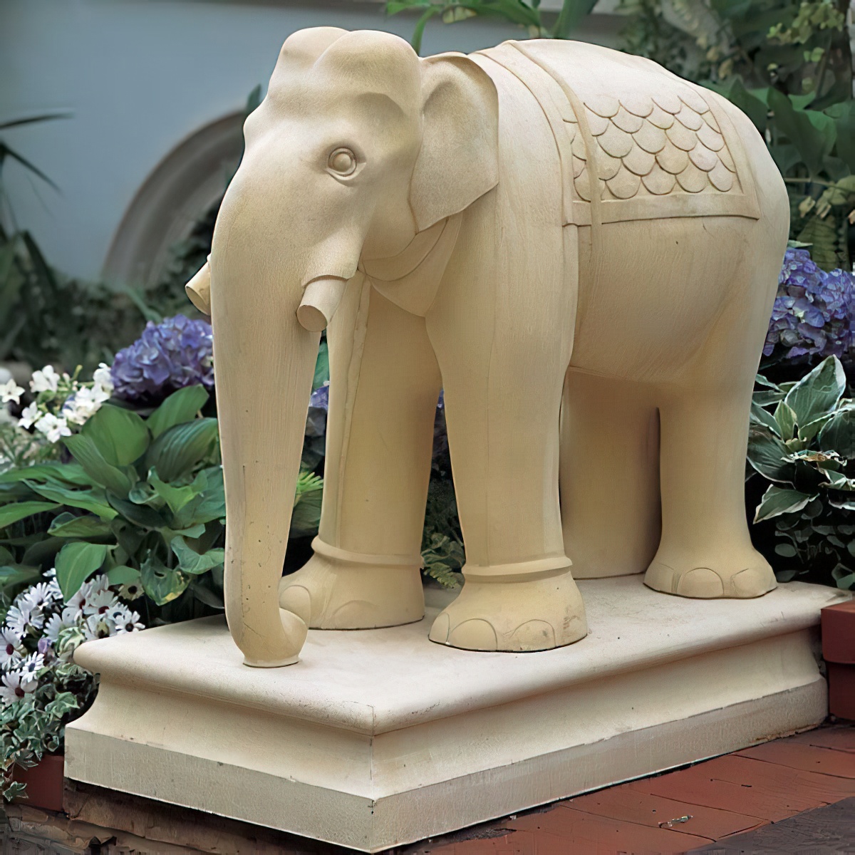 Figura di elefante beige decorativa su un piedistallo nel giardino tra le piante