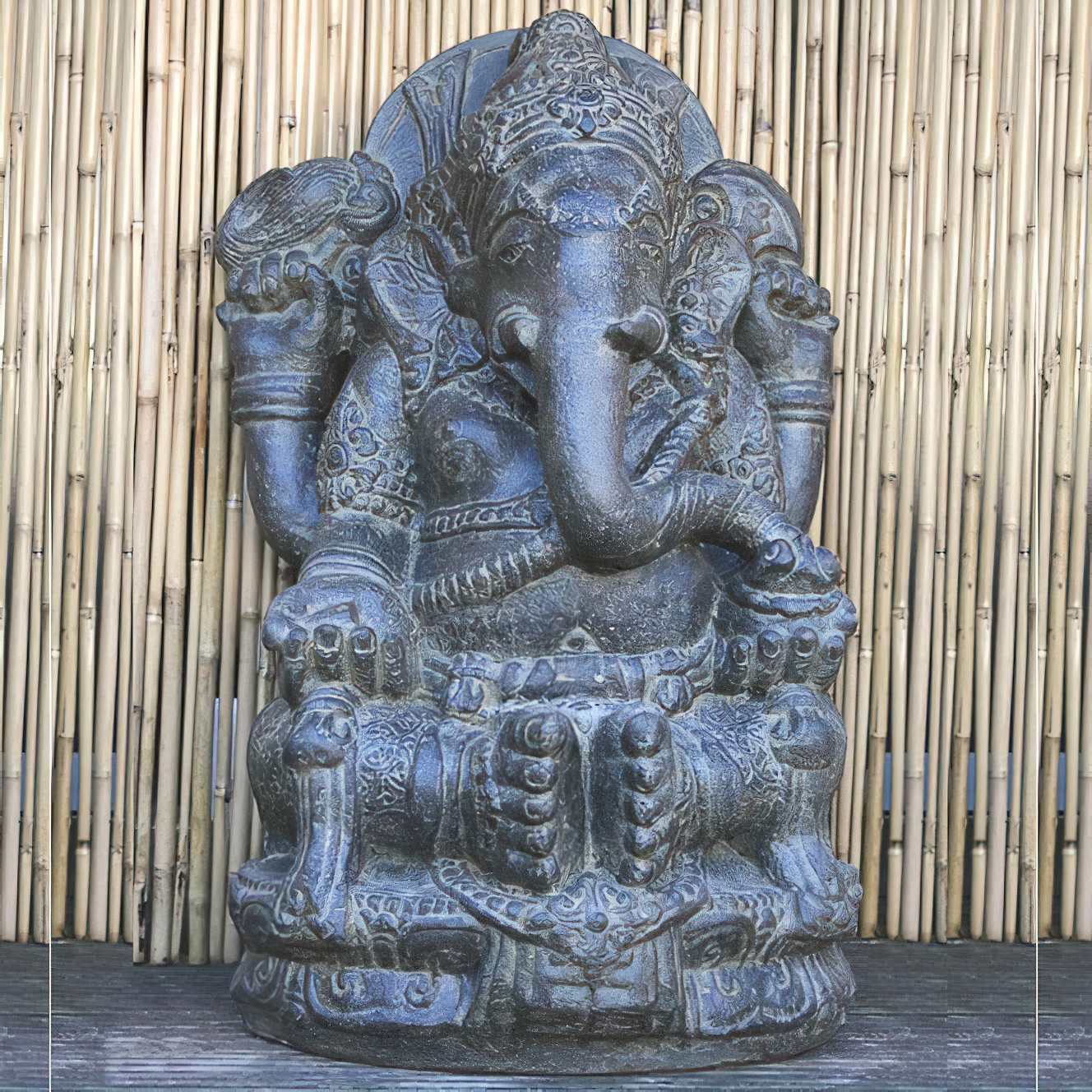 Statue en pierre de Ganesha placée devant un mur de bambou dans un jardin