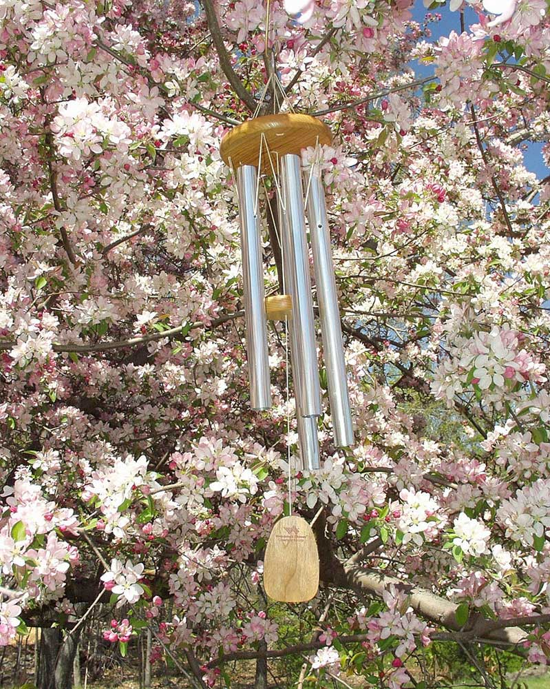 Carillon éolien en métal et bois suspendu à un arbre fleuri dans le jardin