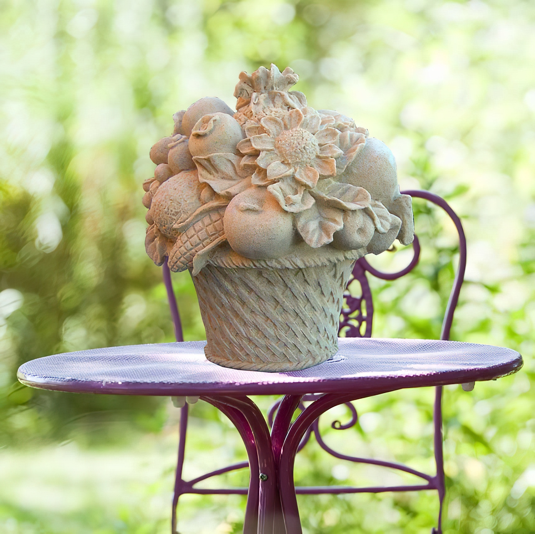Sculpture en forme de panier rempli de fleurs et fruits sur une table de jardin violette entourée de verdure