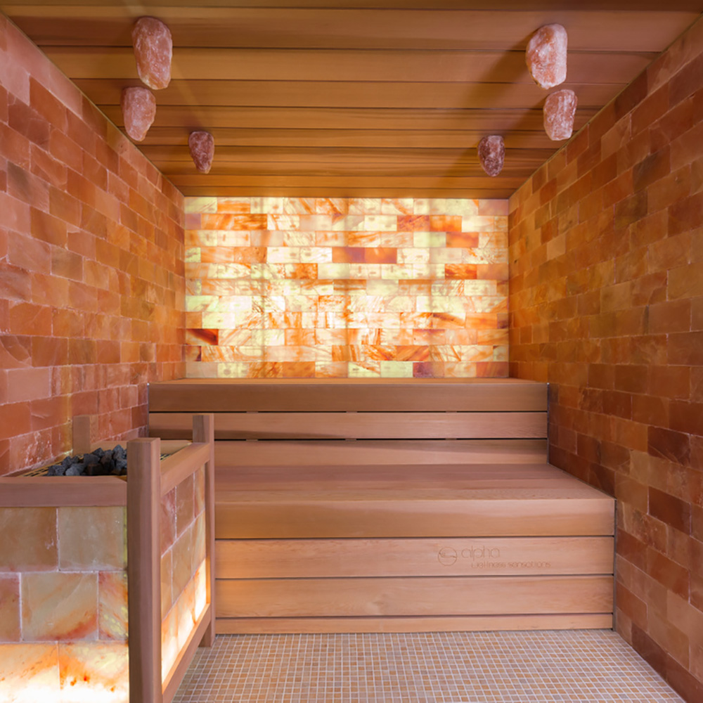 Vista interna di una sauna con pareti in pietra di sale illuminate e panchine in legno