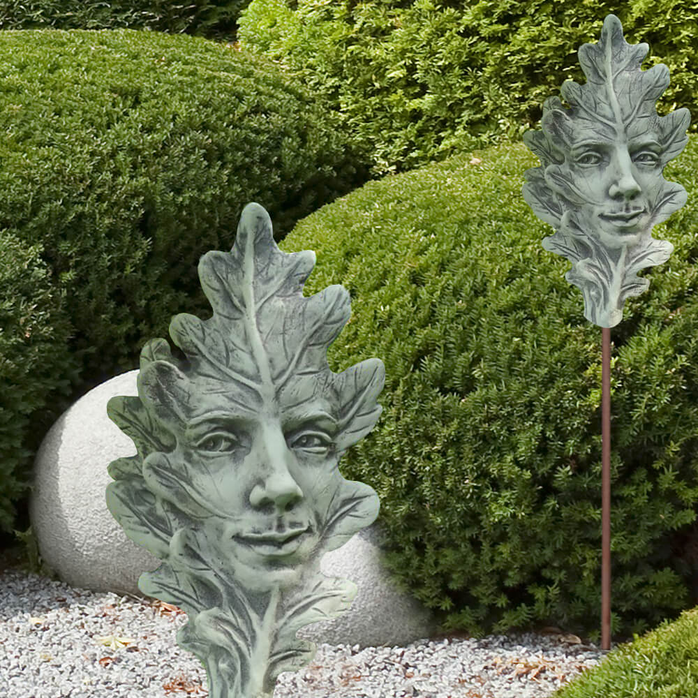 Cadran solaire en métal en forme de feuille avec un visage dans un jardin devant des buissons verts