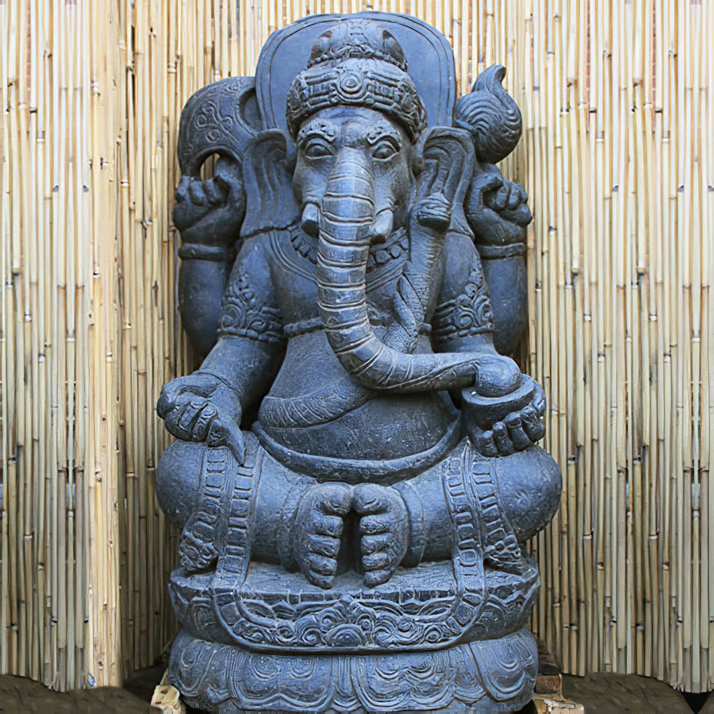 Statue en pierre du dieu Ganesh à tête d'éléphant utilisée comme décoration de jardin devant un mur en bambou