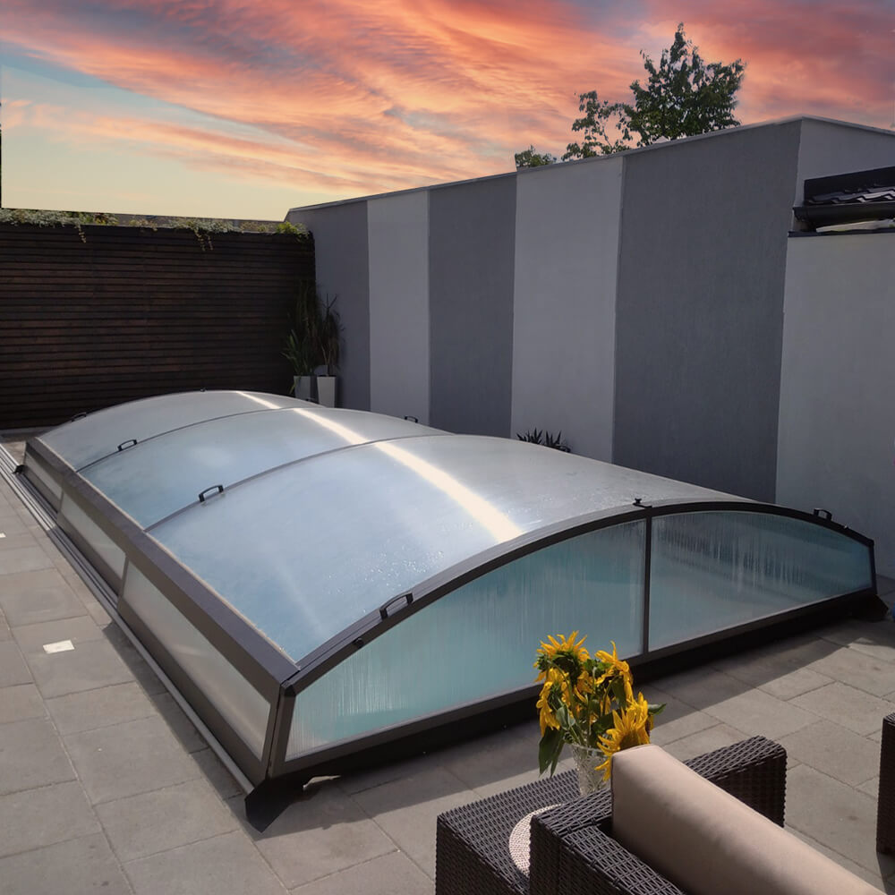 Transparente Poolabdeckung mit Aluminiumrahmen in einem stilvollen Garten am Abendhimmel