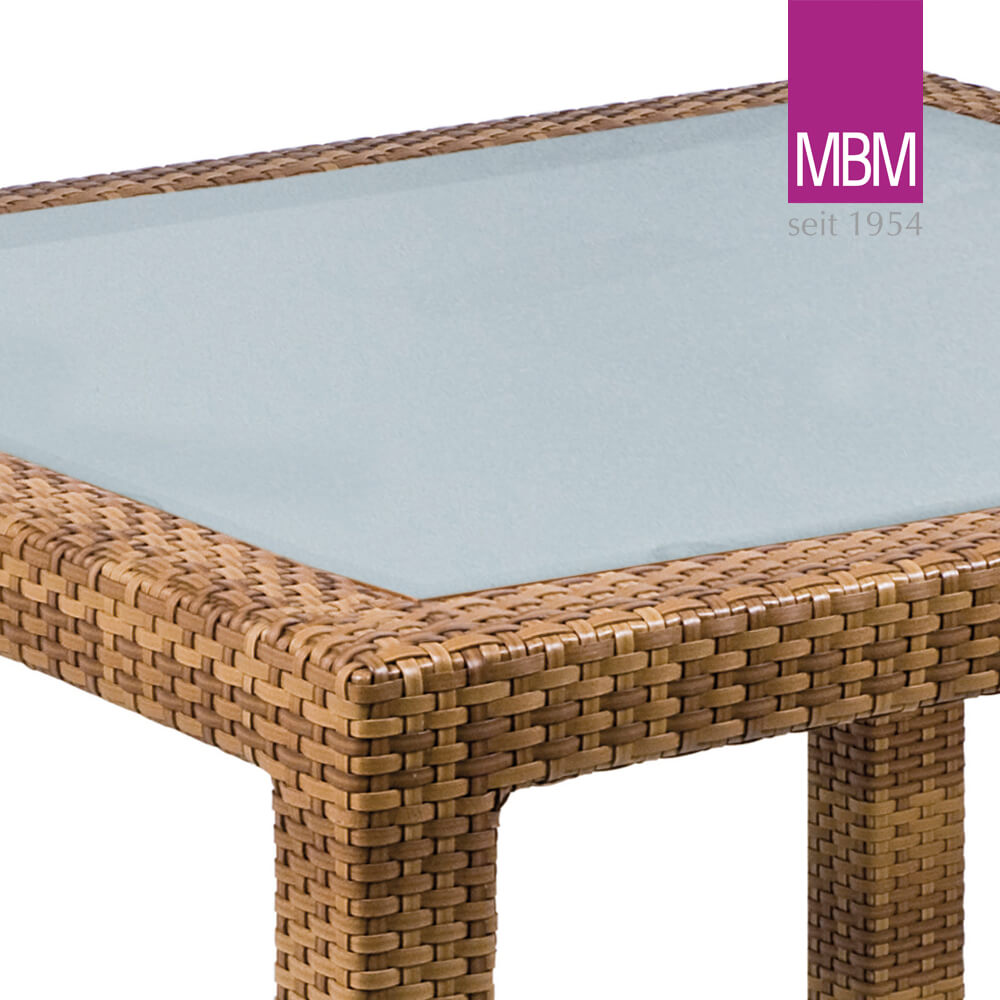 Vue en coin d'une table de jardin en matière tressée avec plateau en verre