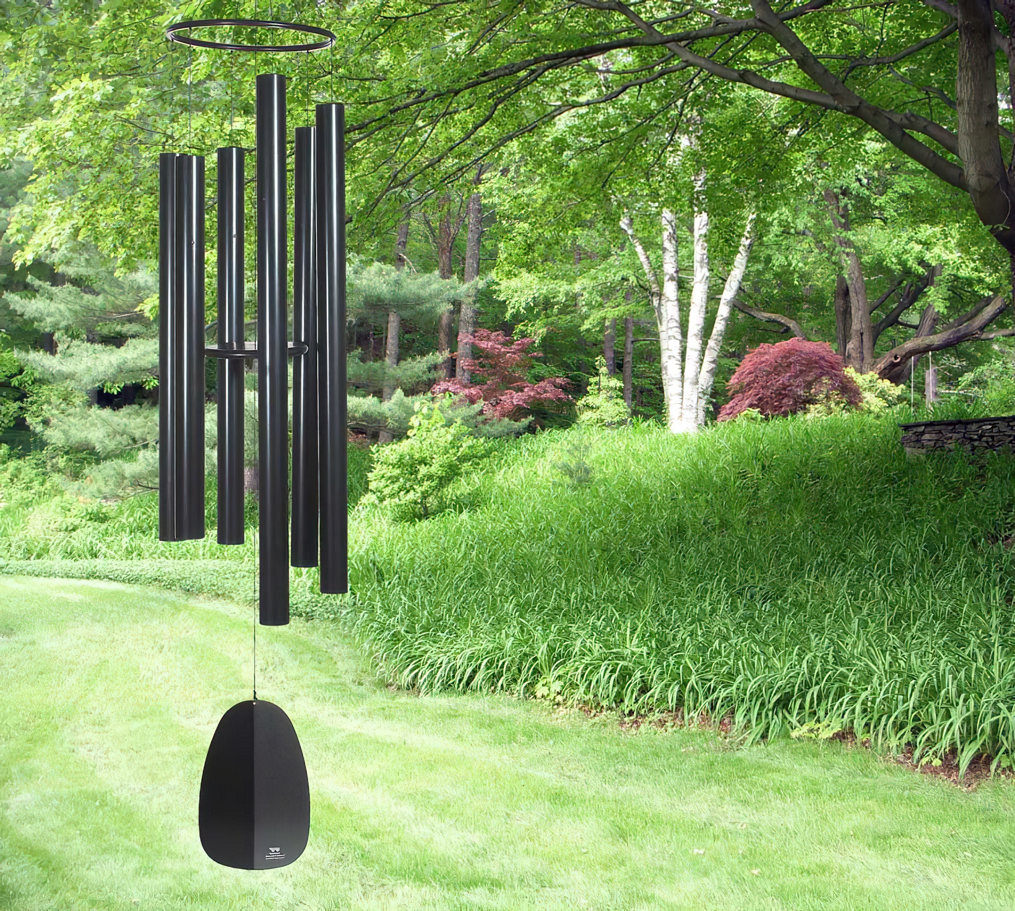 Campanello in metallo nero appeso in un giardino verde con alberi e prato