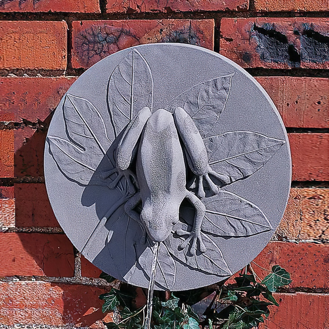 Gartenwandbrunnen mit grauem Frosch und Blättern aus Stein vor roter Backsteinmauer