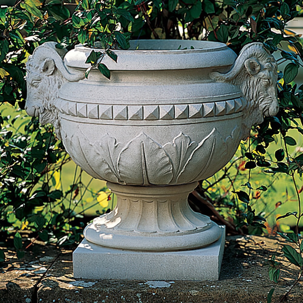 Großer Steinblumentopf mit Widderkopf-Motiv, umgeben von Grünpflanzen im Garten
