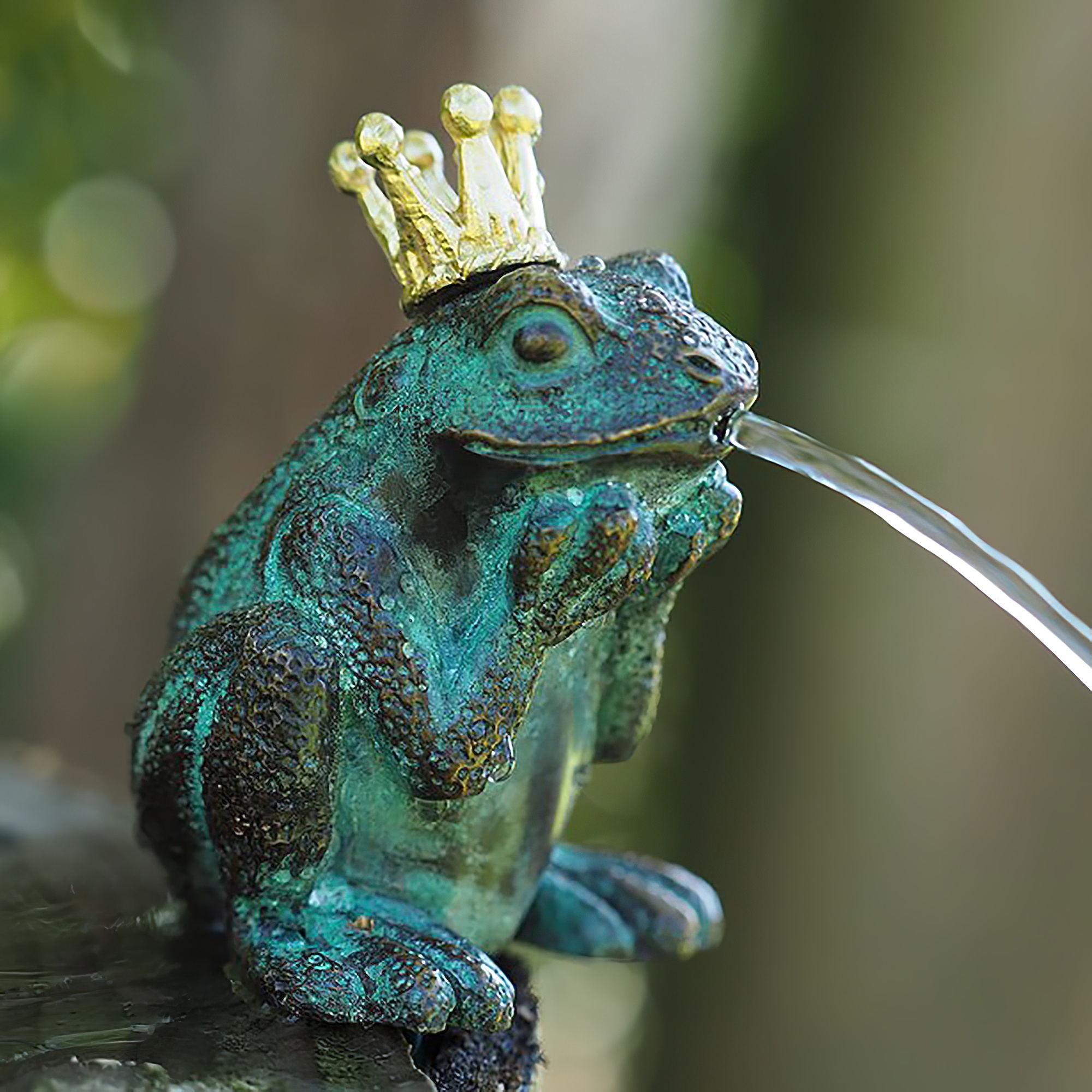 Detailbild eines grünen Frosches mit goldener Krone, der als Gartenbrunnen Wasser speit