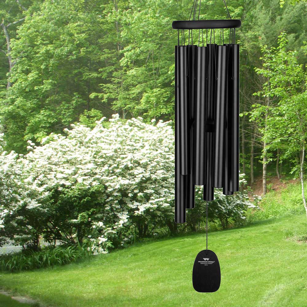 Grand carillon à vent noir suspendu dans un jardin vert devant un buisson en fleurs
