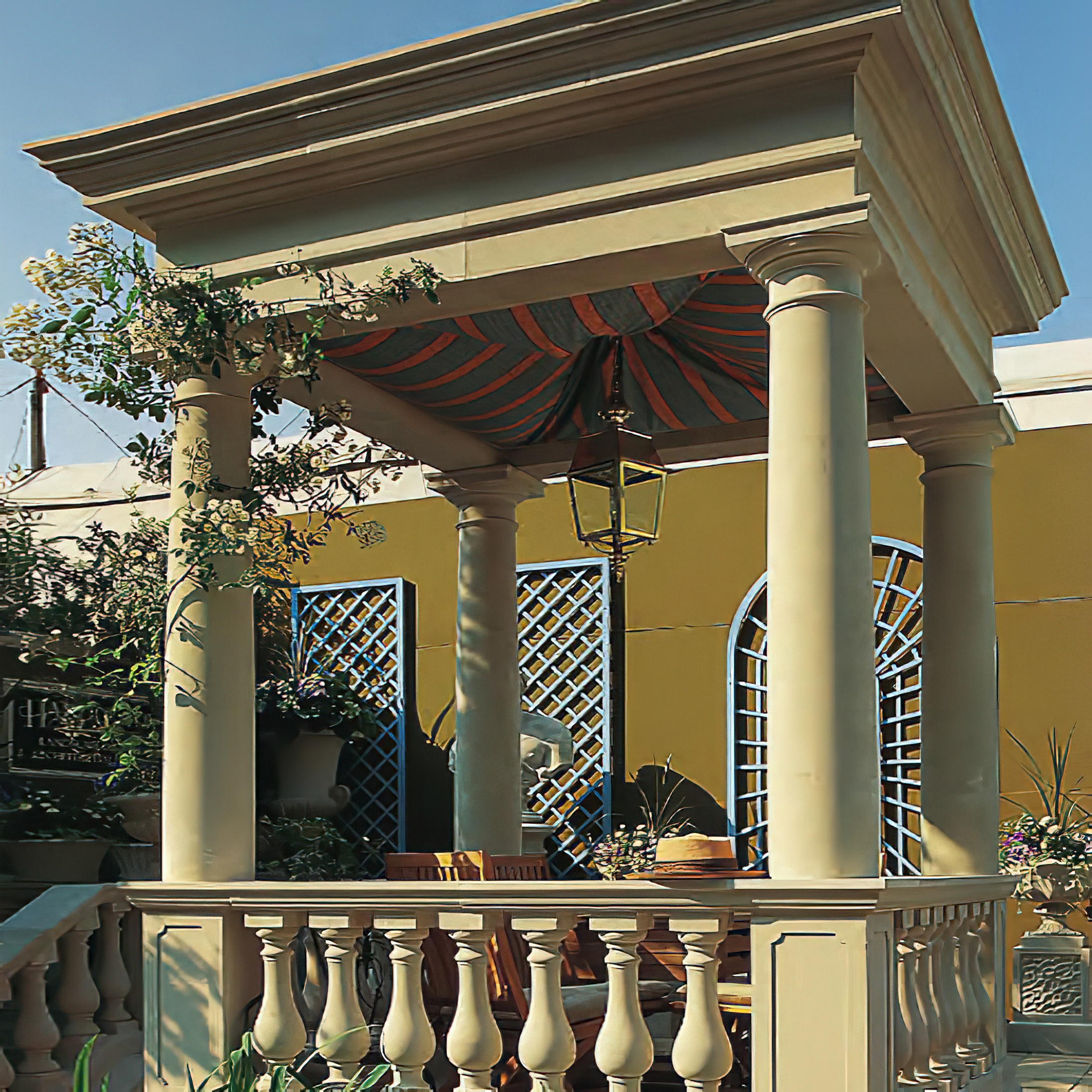 Pavillon de jardin avec colonnes et parasol devant un mur jaune