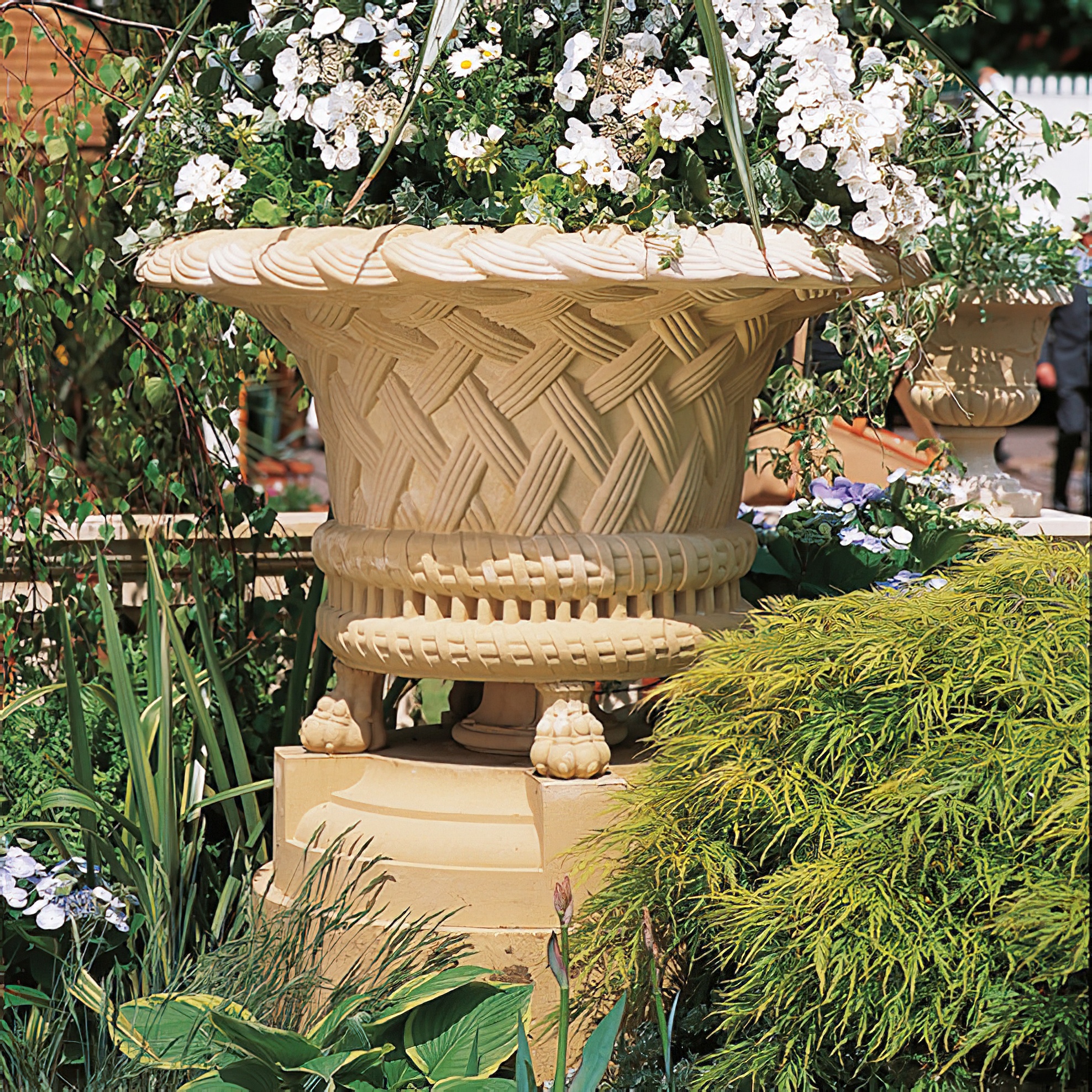 Grande jardinière en pierre avec des fleurs blanches dans un jardin avec des plantes vertes