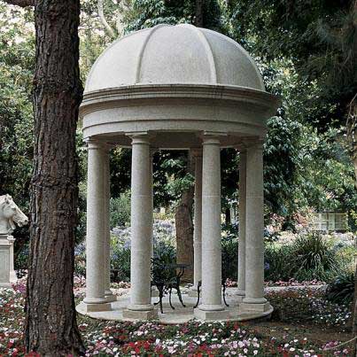 Weißer steinerner runder Pavillon mit Säulen im Garten umgeben von Bäumen und Blumen