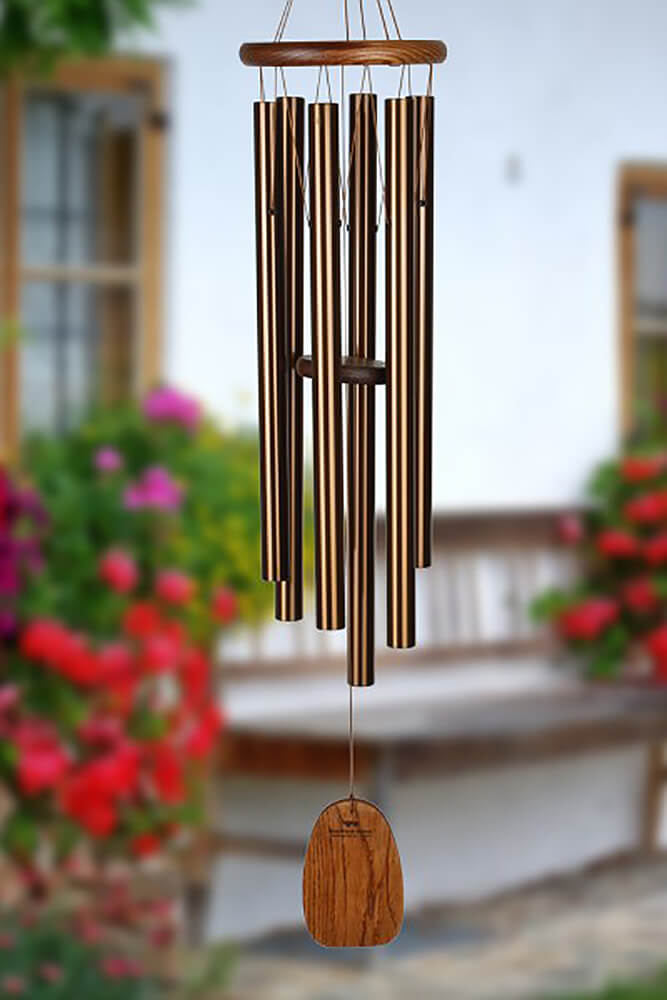 Carillon en tubes d'acier inoxydable et bois dans un jardin devant des fleurs et une maison