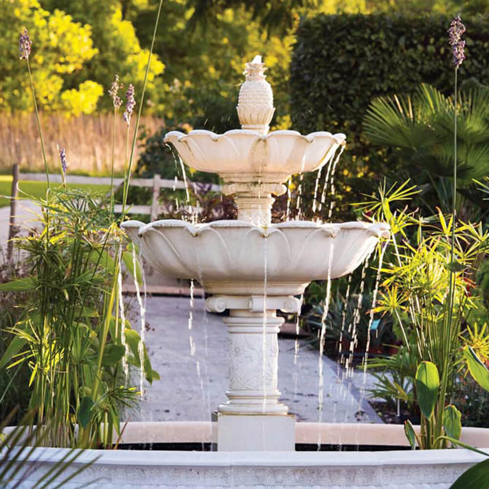 Weißer Steinbrunnen mit mehreren Wasserstrahlen in einem sonnigen Garten