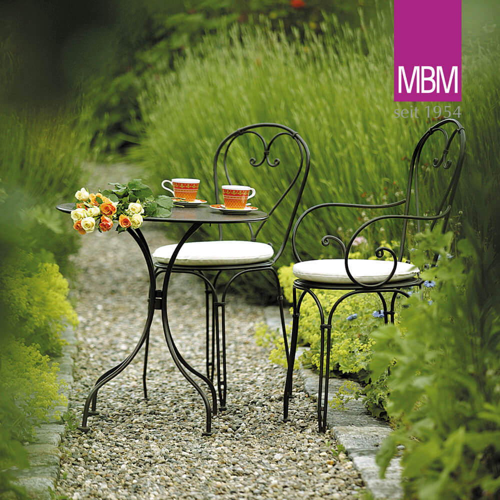 Tavolo da giardino in metallo nero con due sedie imbottite su sentiero di ghiaia in un giardino verde