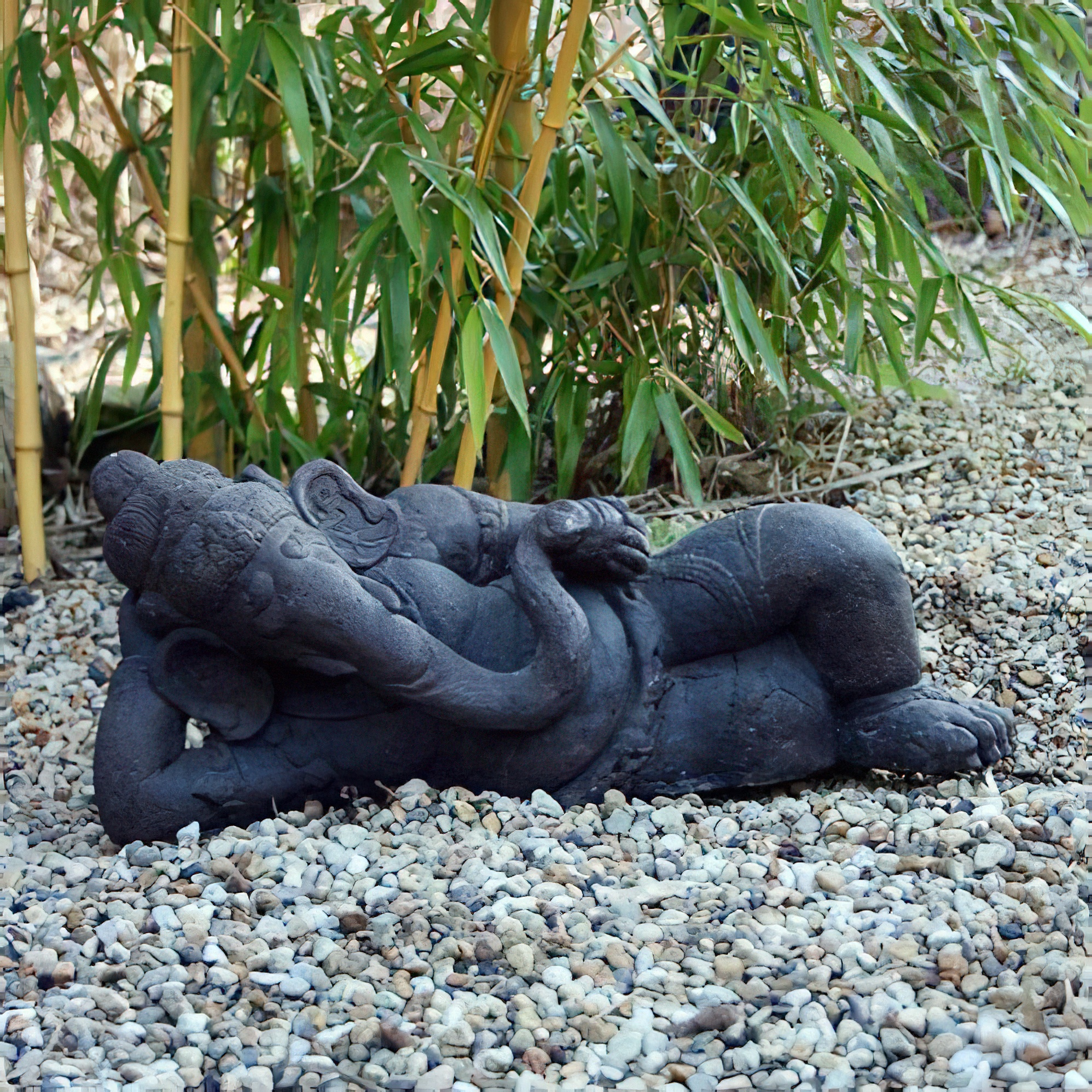 Figure de Bouddha noire allongée en pierre sur des cailloux dans le jardin