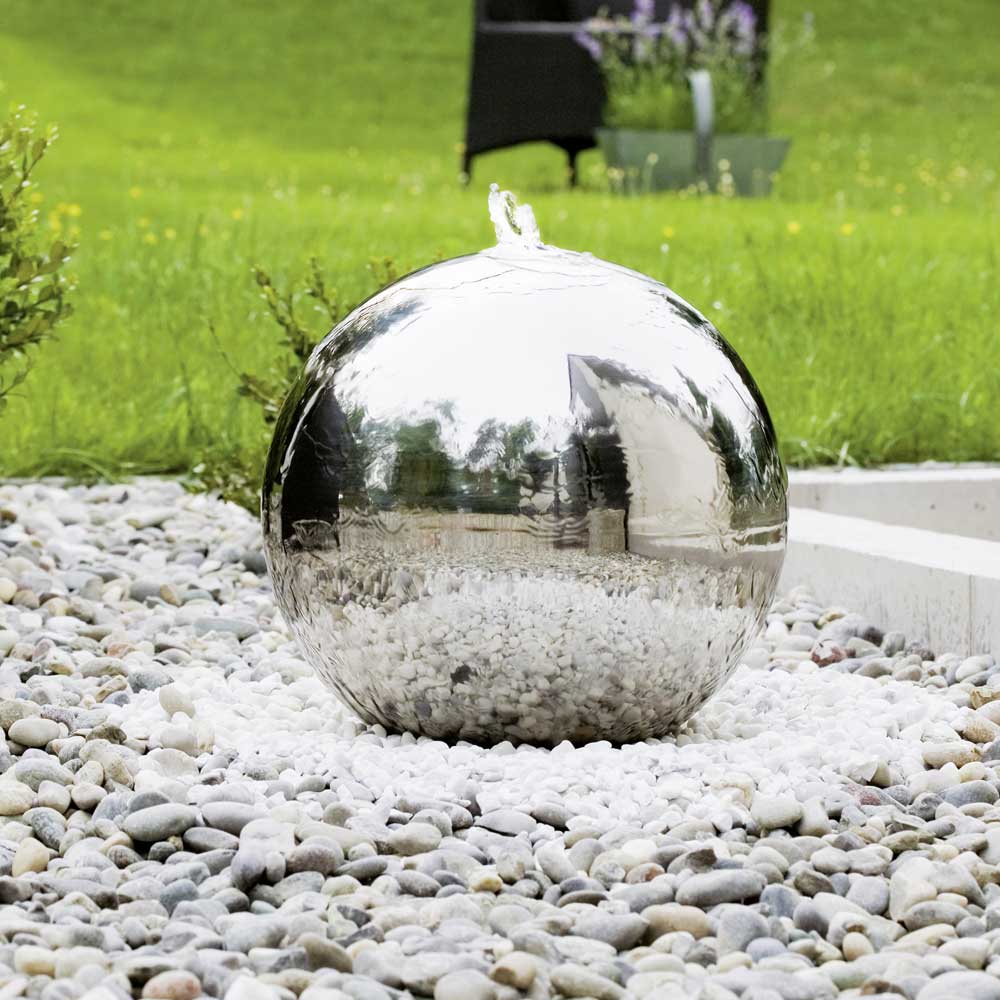 Sphère miroir en acier inoxydable décorant un jardin avec des cailloux et de l'herbe verte