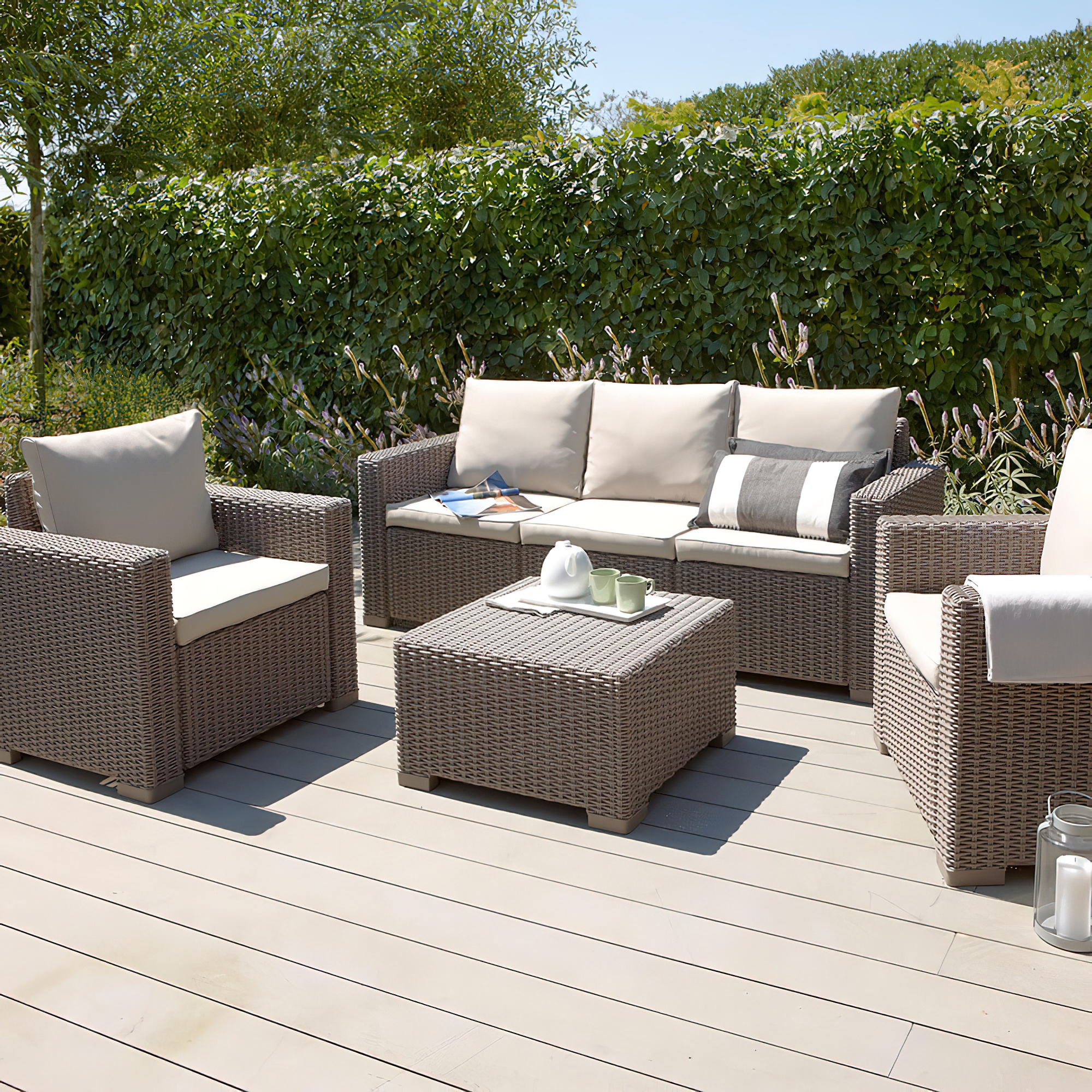 Set lounge beige in polyrattan con divano, poltrone e tavolino su terrazza in legno nel giardino