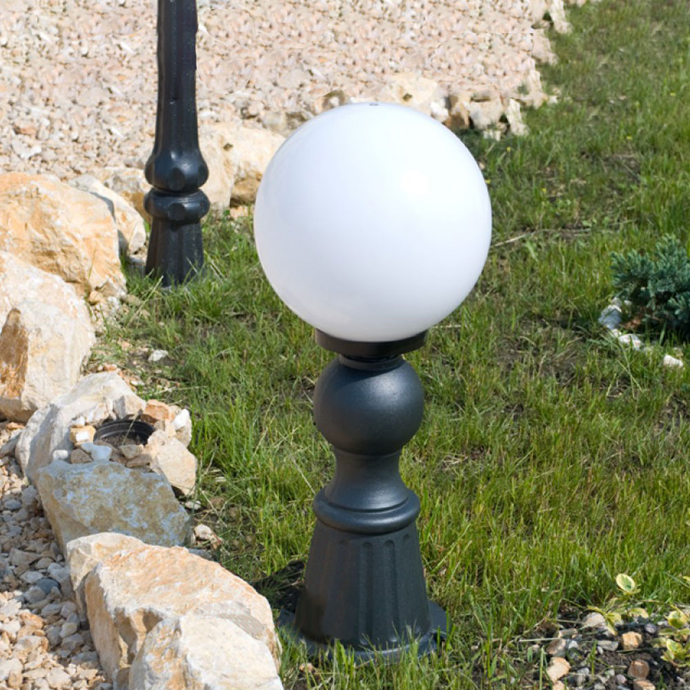 Kugelförmige Außenlampe auf schwarzem Sockel im Garten neben Steinweg