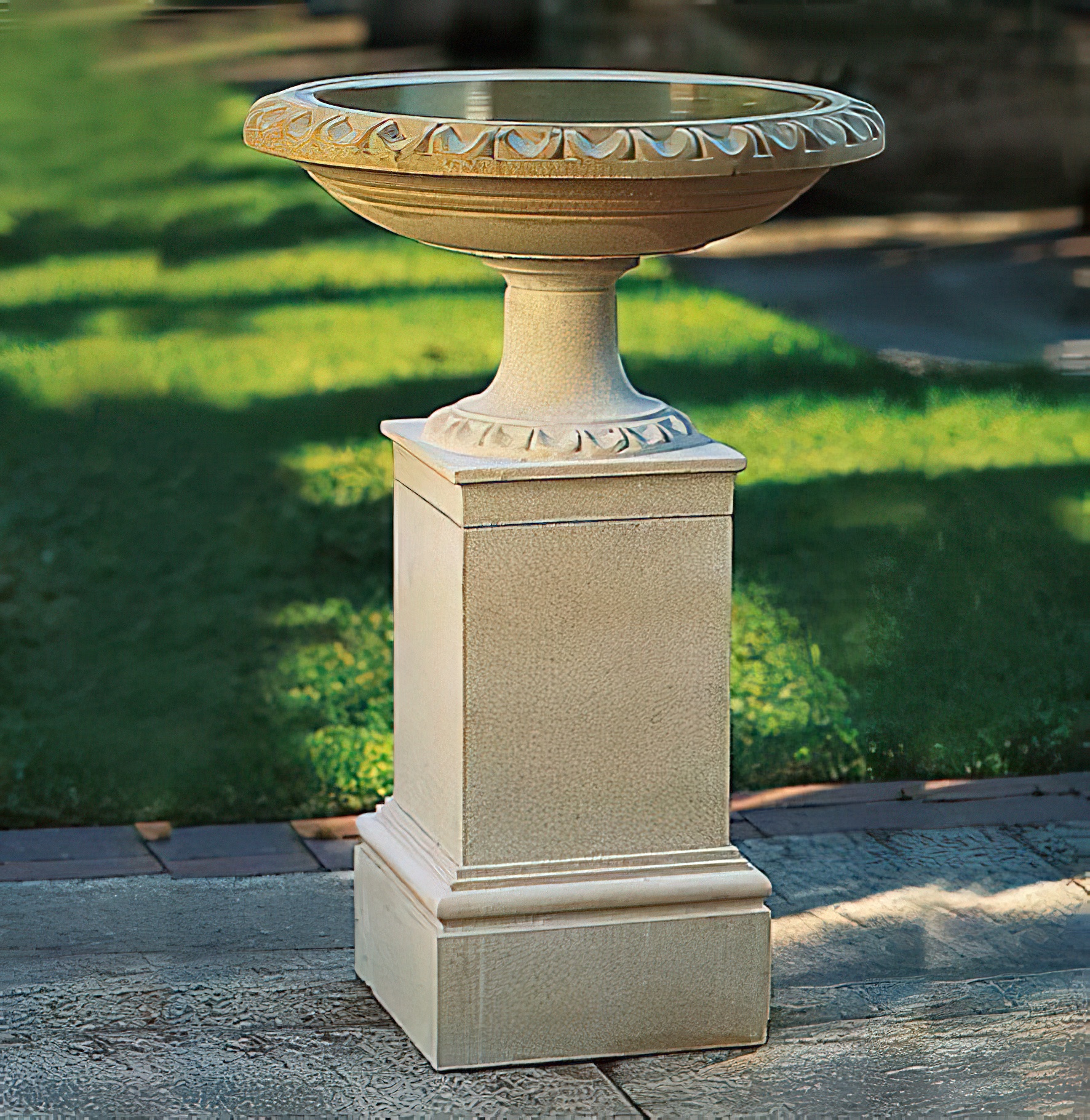 Steinerner Gartenbrunnen auf einem quadratischen Sockel in einem grünen Garten