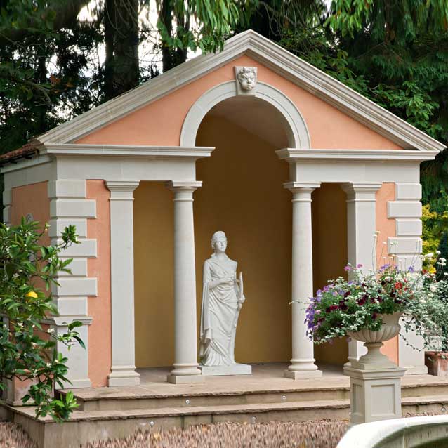 Ein elegantes Gartenhaus mit vier Säulen und einer Statue in der Mitte, umgeben von grünen Pflanzen