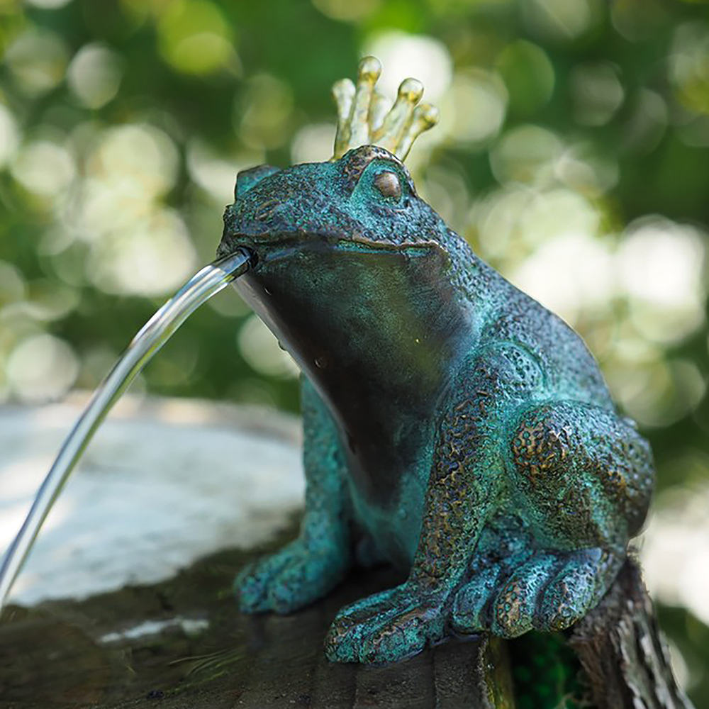 Grüne Froschfigur mit Krone, die Wasser in den Garten spritzt