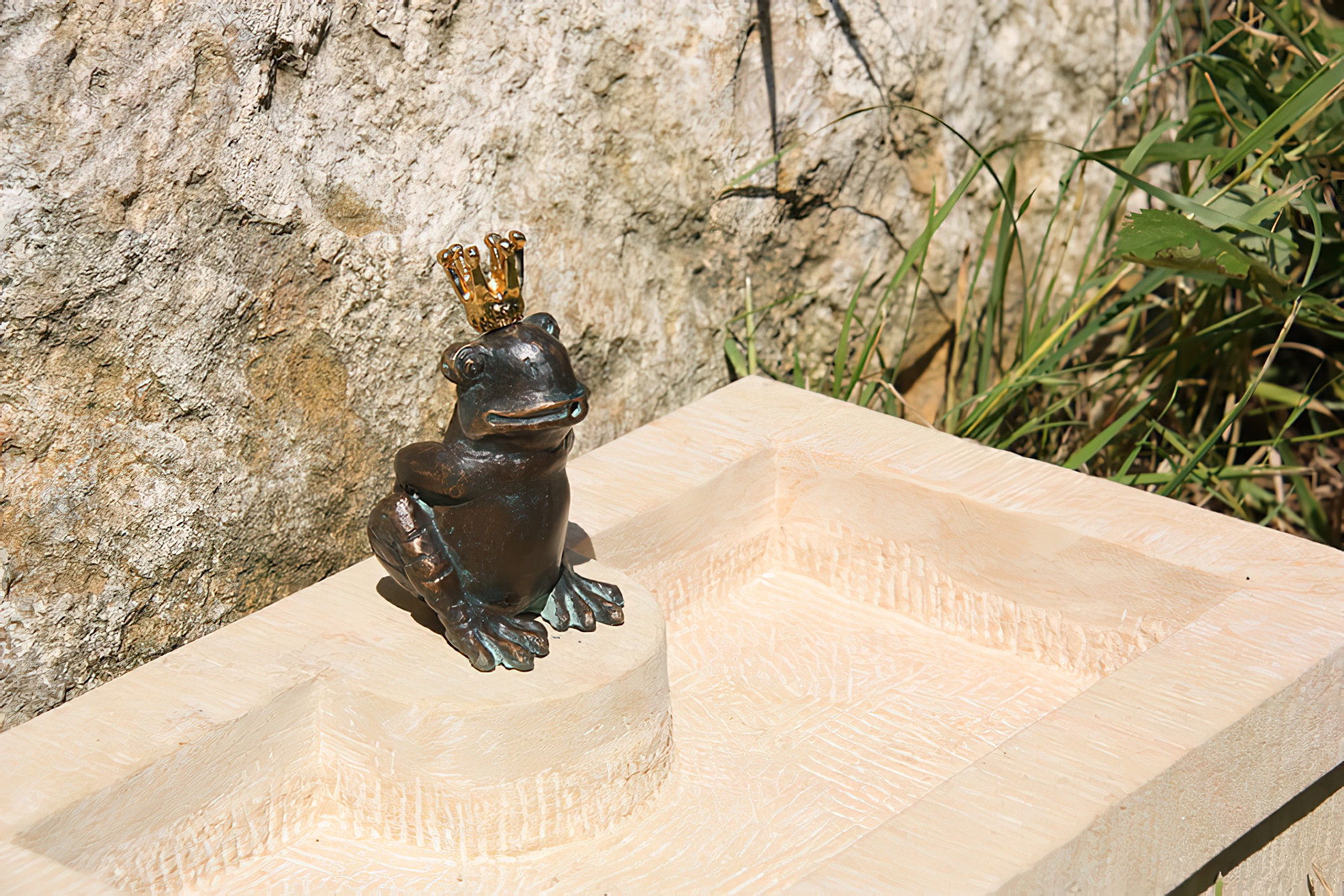 Fontana in pietra con figura di ranocchio reale in bronzo in un giardino davanti a un muro di pietra