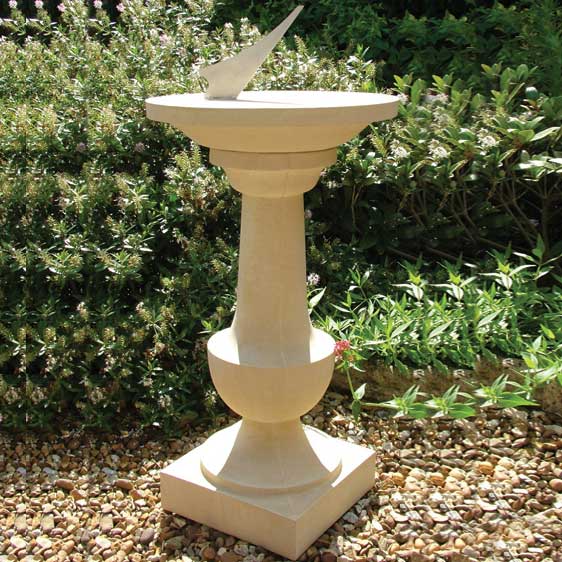 Cadran solaire en pierre sur colonne dans un jardin parmi des plantes et des cailloux