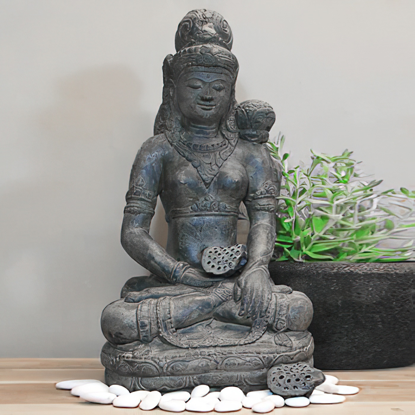 Figure de Bouddha en pierre sur surface en bois avec pierres décoratives et plante en arrière-plan