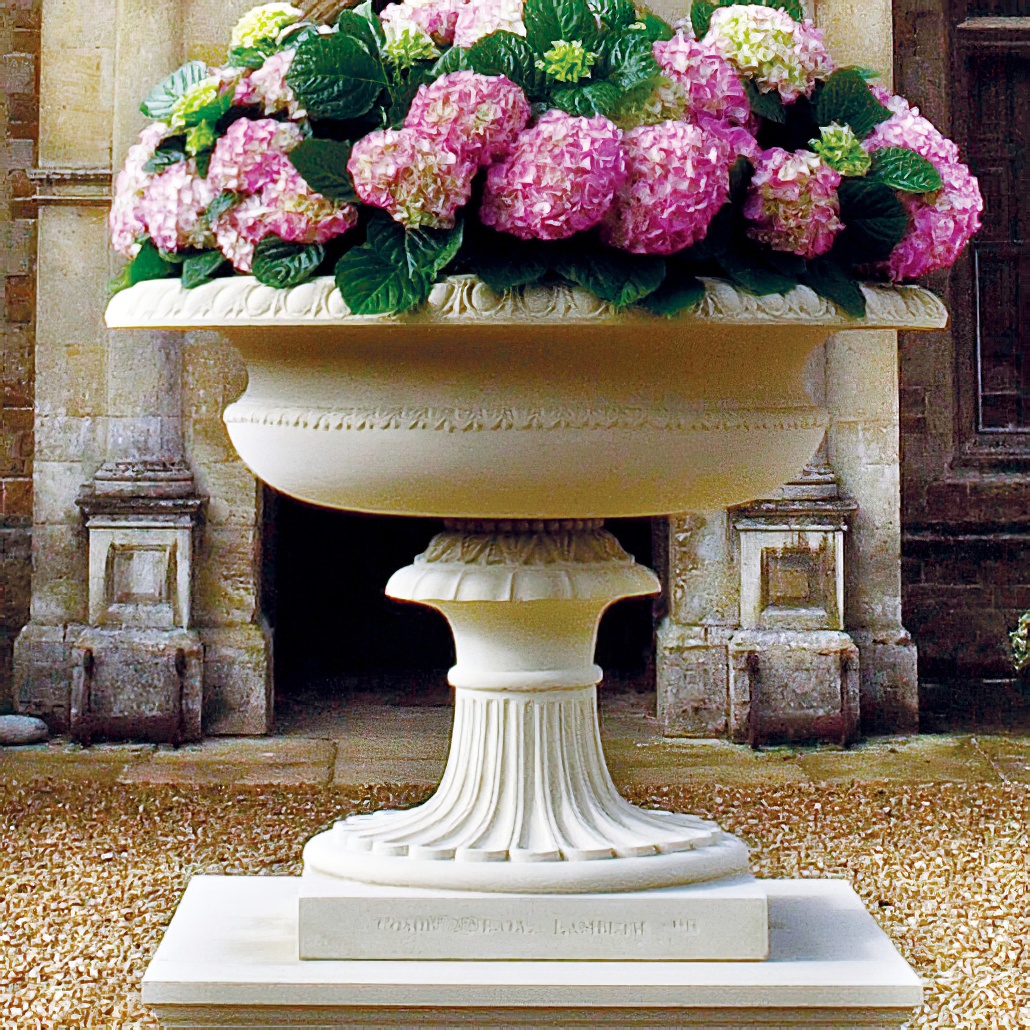 Weisser, antiker Steinblumenkübel mit rosa Hortensien als Garten-Dekoration