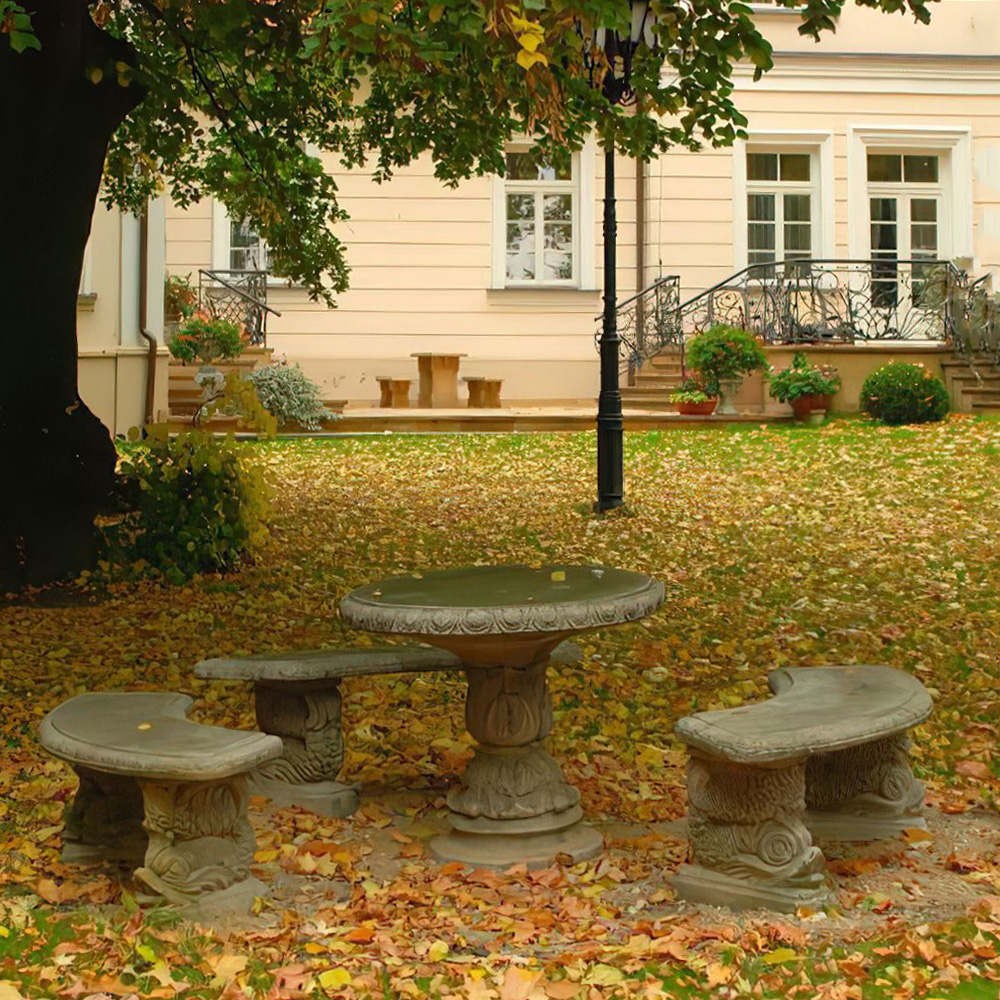 Rustikaler Steintisch mit Bänken umgeben von Herbstblättern im Garten vor einem Haus