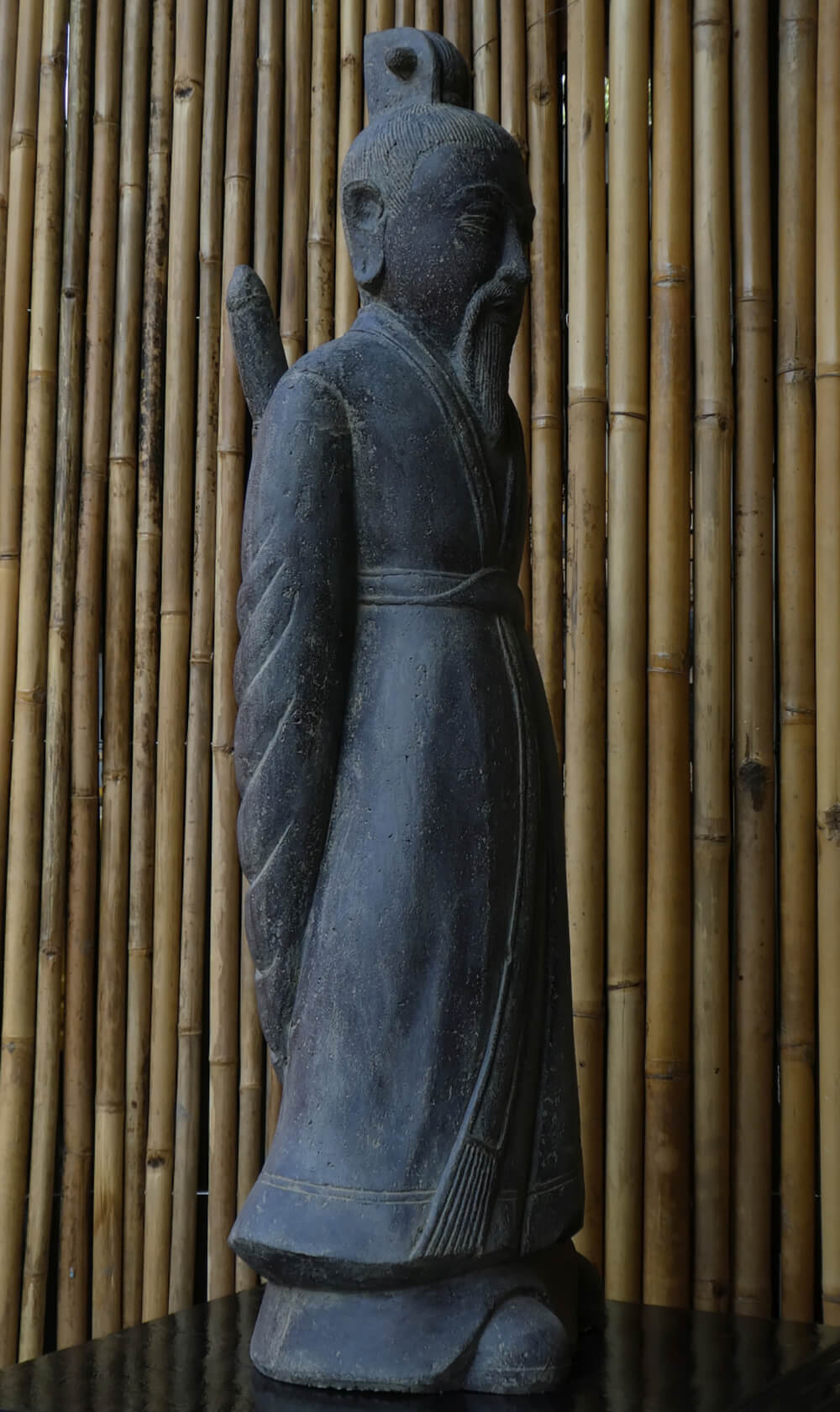 Statue asiatique en pierre foncée devant un fond en bambou pour décoration de jardin exclusive