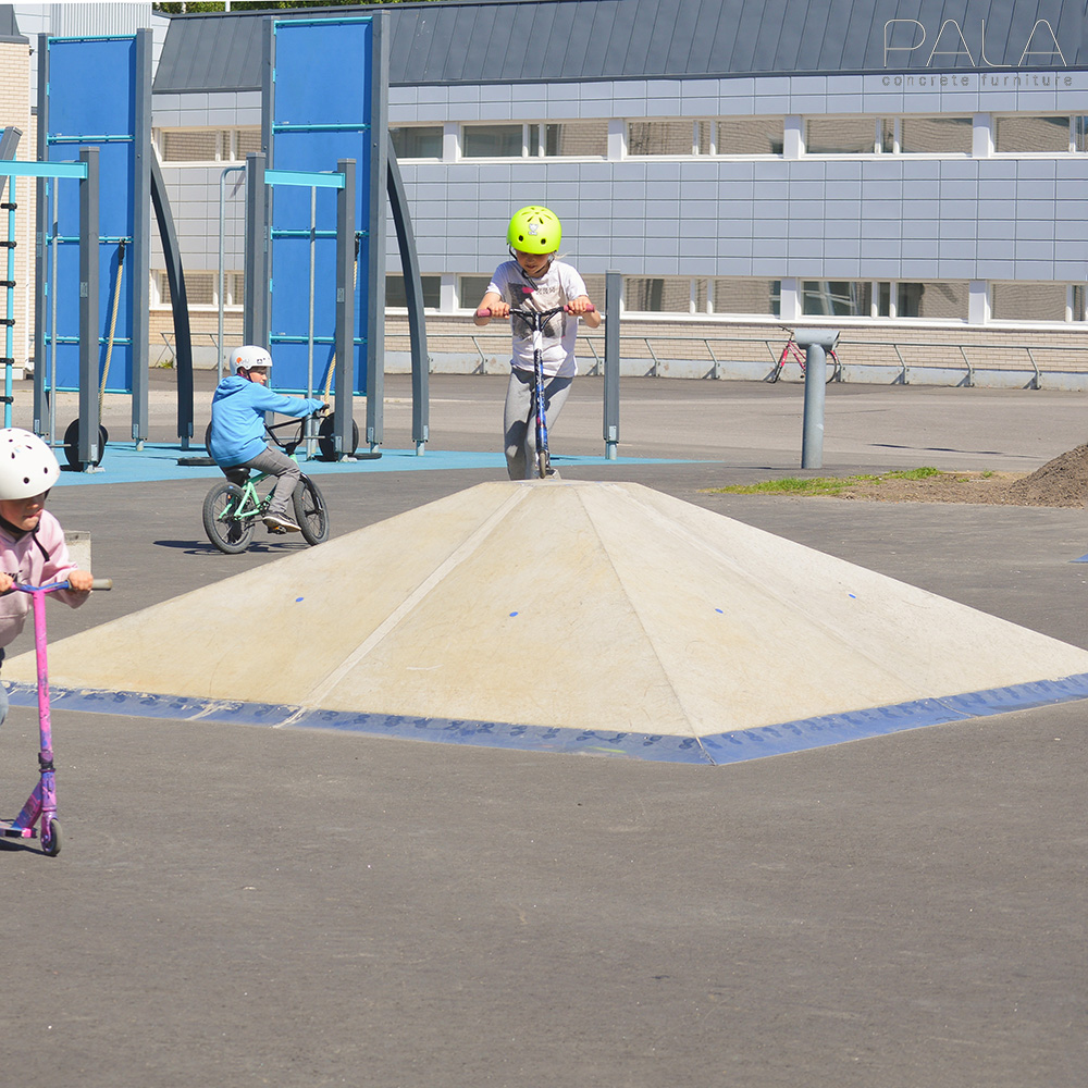 Tre bambini giocano con monopattini su una pista con una piccola rampa in cemento