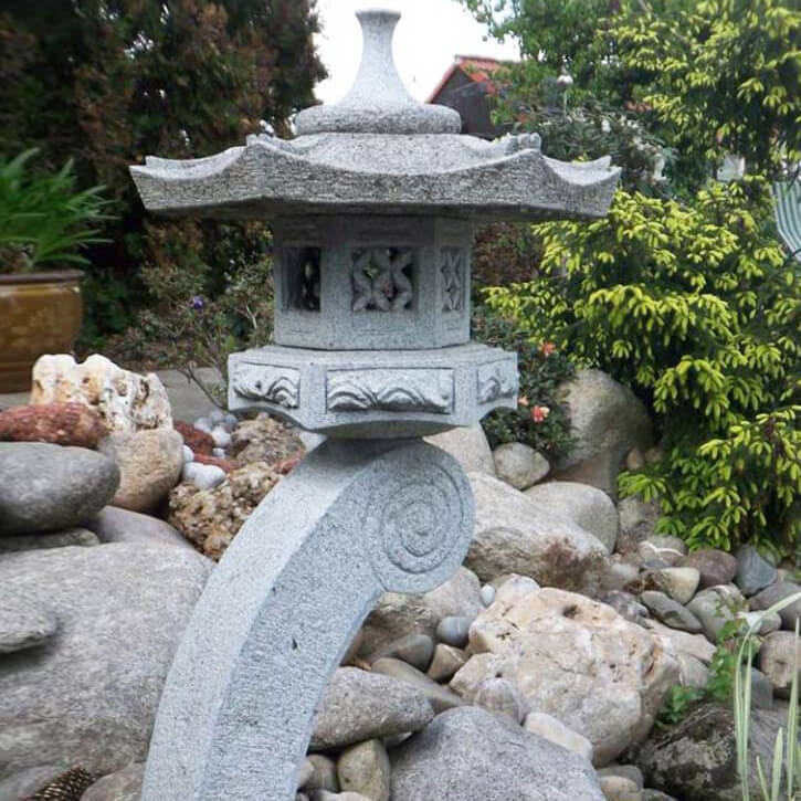 Elegante japanische Steinlaterne als Gartendeko zwischen Steinen und Pflanzen