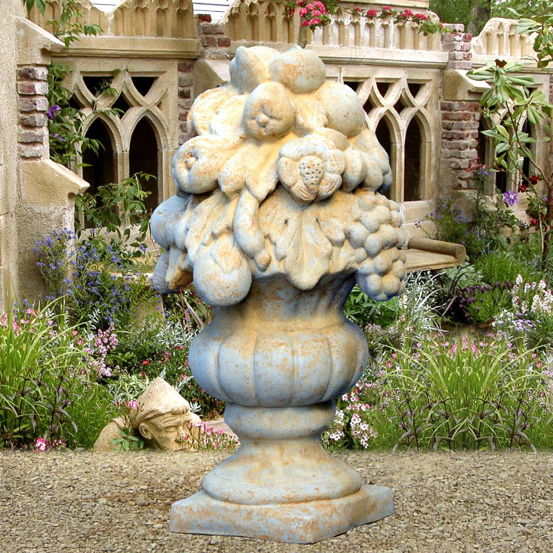 Vase en pierre orné de motifs de fruits et feuilles dans un jardin devant un bâtiment ancien
