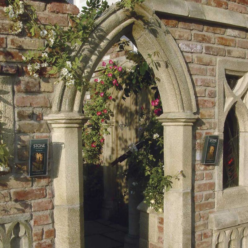 Portail en arc en pierre dans un jardin avec des fleurs et un mur en briques